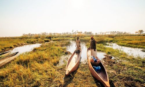 2 people in wooden canoes in the Okavango delta
