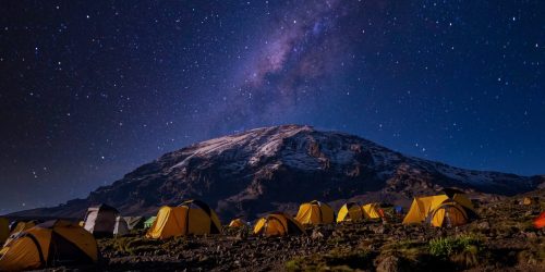 Yellow tents set up on Kilimanjaro at night with starry sky in background