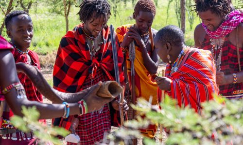 masai warrior dressed in traditional clothing showing his friends something