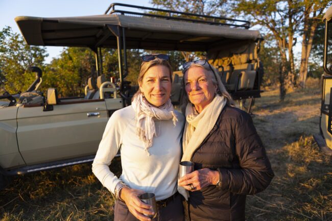 Adult woman and her mother standing side by side, by a jeep at sundown