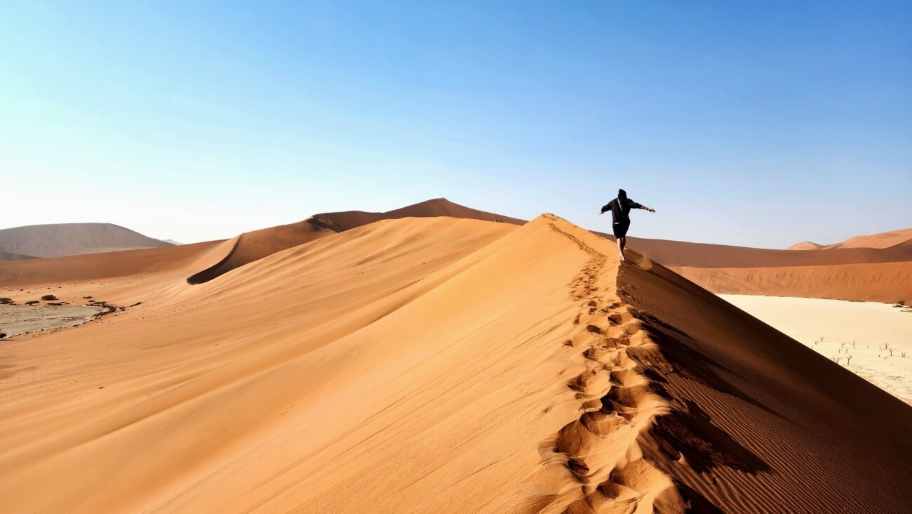Man running along top of dune in Namibian desert.