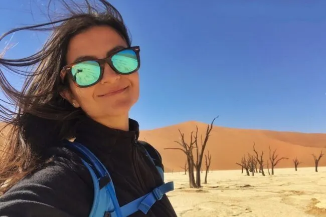 Woman smiling in the desert with dunes and trees in the background