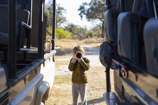 Young boy with camera on safari taking picture of vehicle from outside, Okavango Delta, Botswana