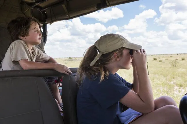 Young brother and sister in safari vehicle looking for animals.