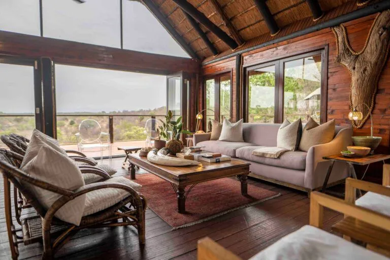 inside of a lounge area with couches and a coffee table with views of the bush outside the window