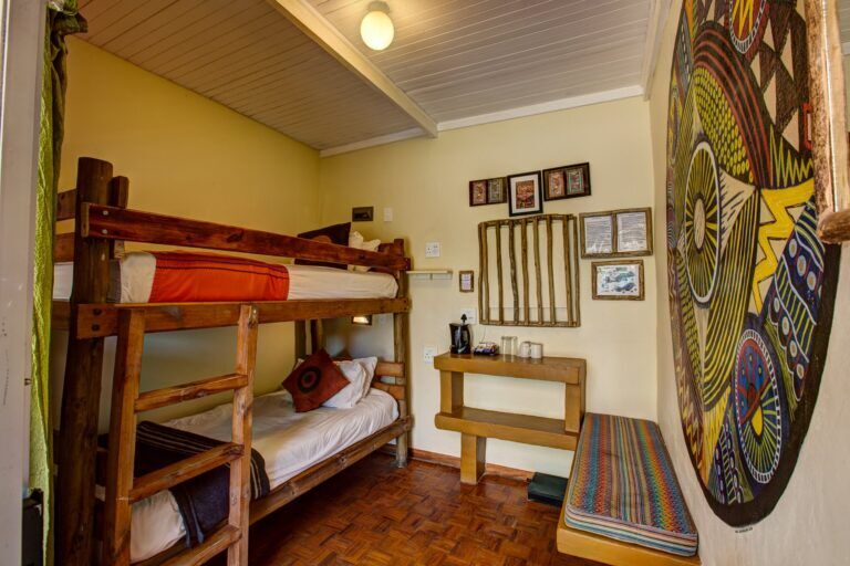 inside of a room with bunk beds, a bench and coffee station with traditional art against the wall