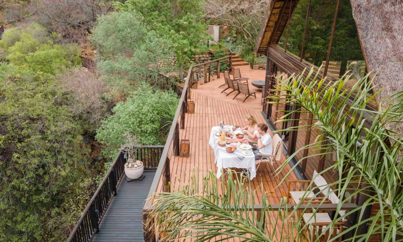 two people sitting down to eat on a patio with the bush as their view