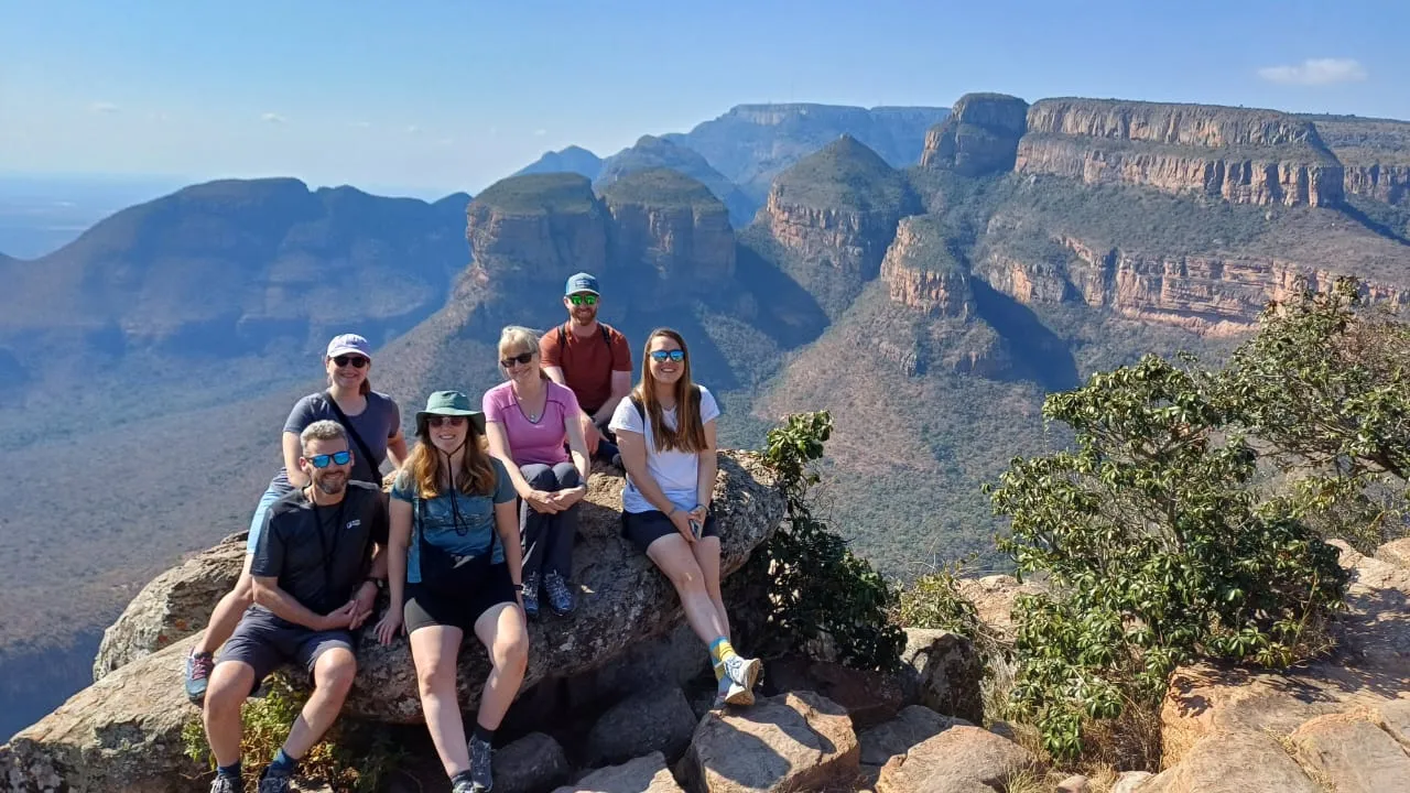 group of people posing on a rock with mountains in the background