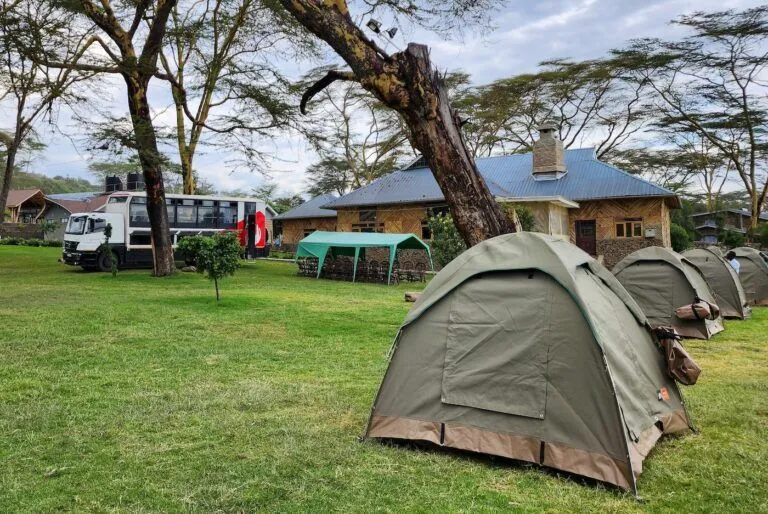 a tour bus, tents and eating area on a grass area with a house behind them