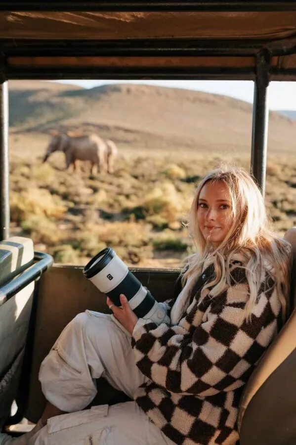 a lady sitting with a big digital camera on a safari vehicle with elephants in the background