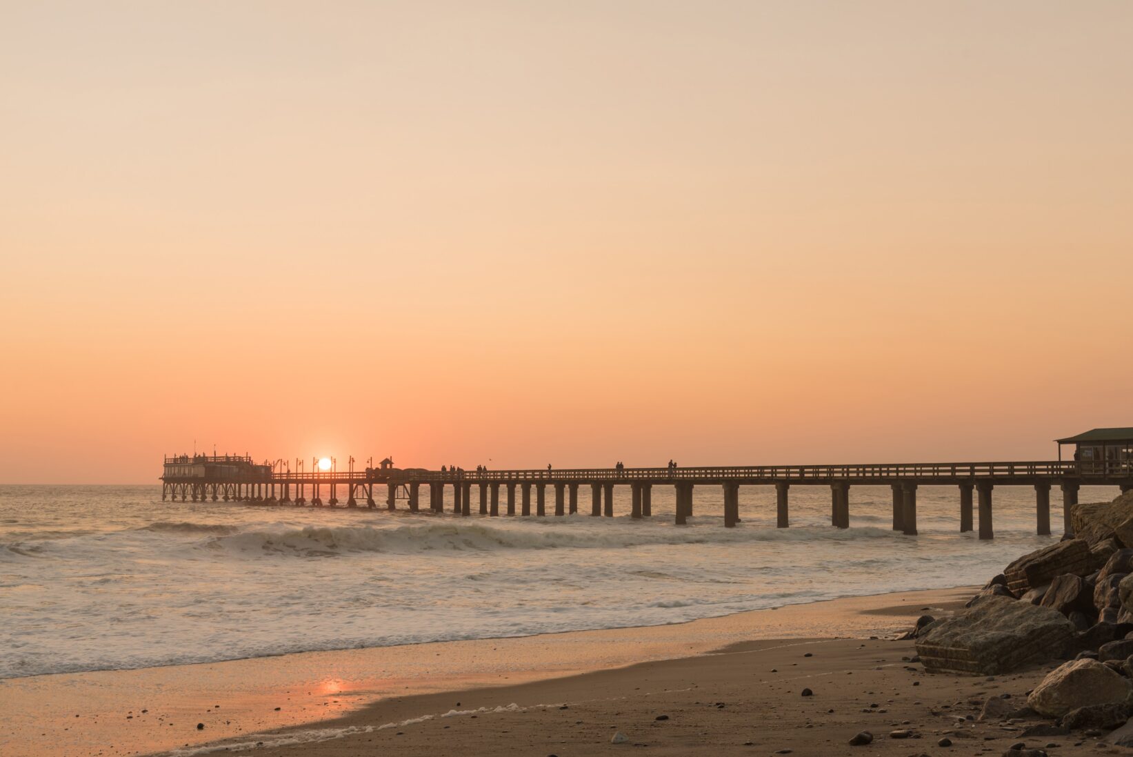 wide angle of a jetty out to sea during sunset with the sea and beach in the background