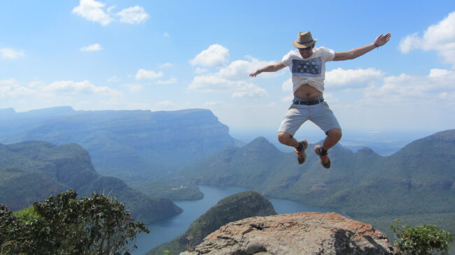 Traveler jumping over rock at Blyde River Canyon viewpoint