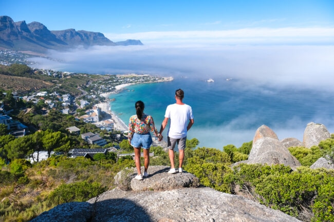 two people holding hands while looking out over camps bay