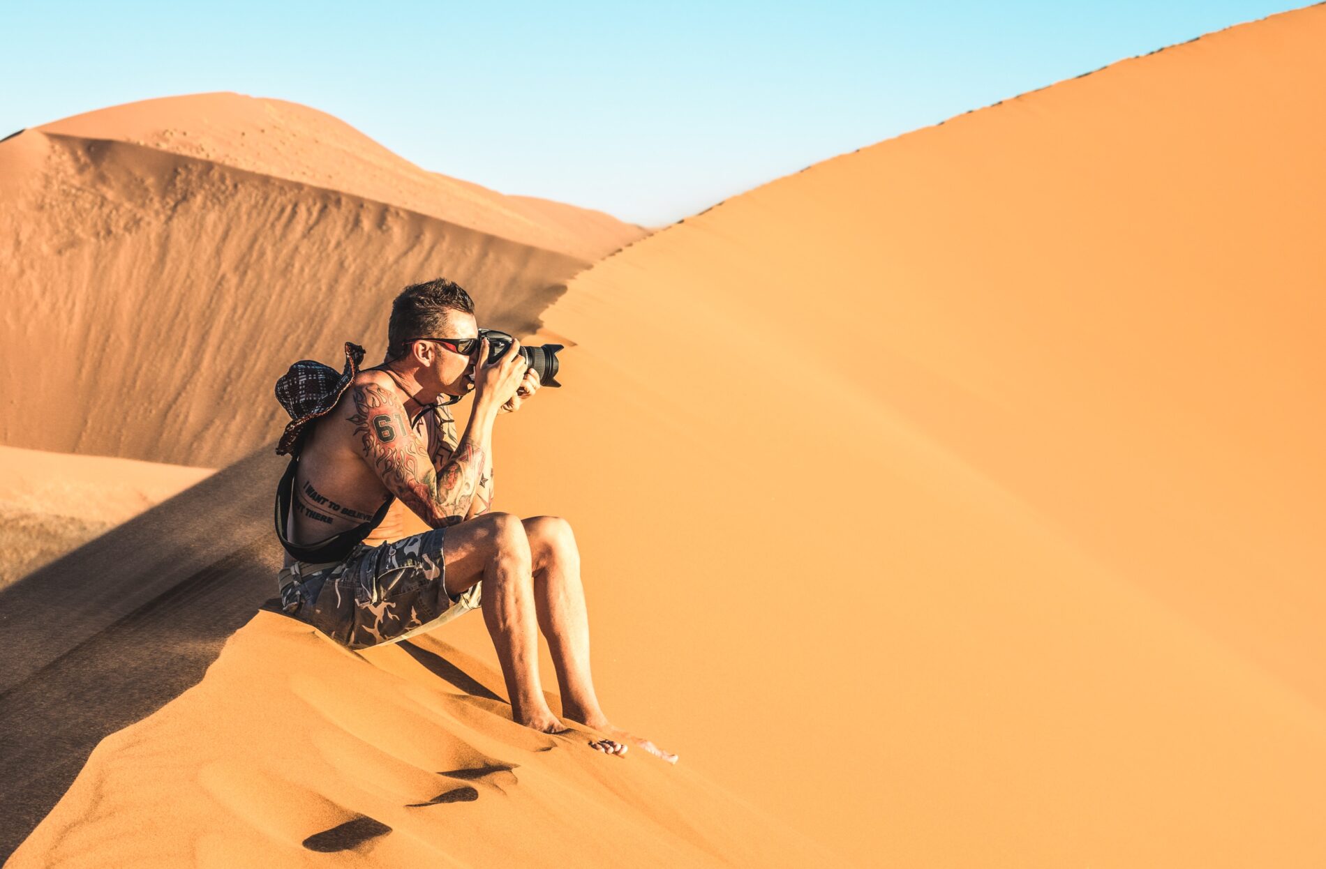 Lonely man photographer sitting on sand at Dune 45 in Sossusvlei Solo man photographer sitting on sand at Dune 45 in Sossusvlei - Adventure travel to African wonders in Namibia