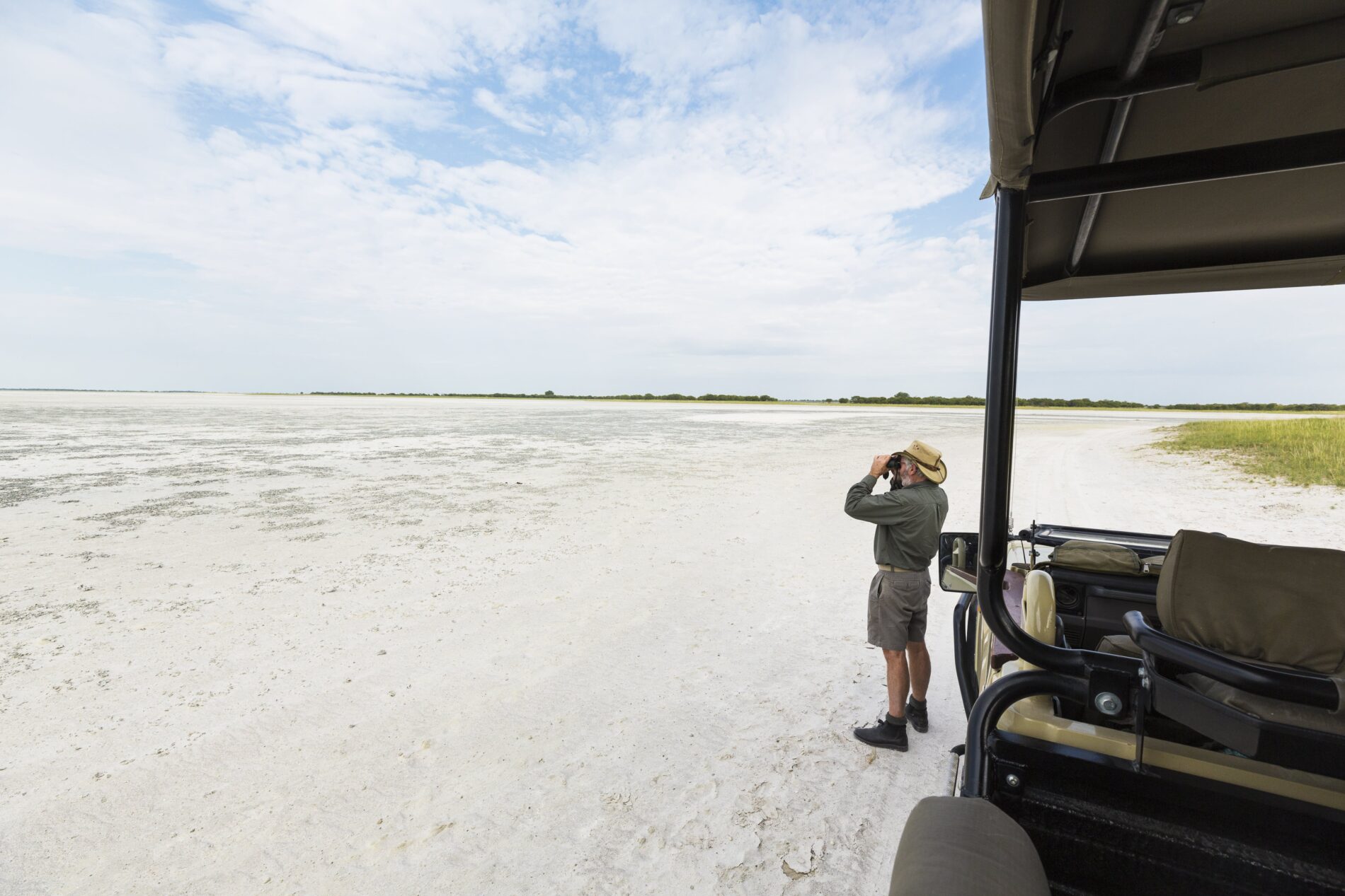 Safari guide looking out at Salt Pan, Botswana with binoculars in front of safari jeep