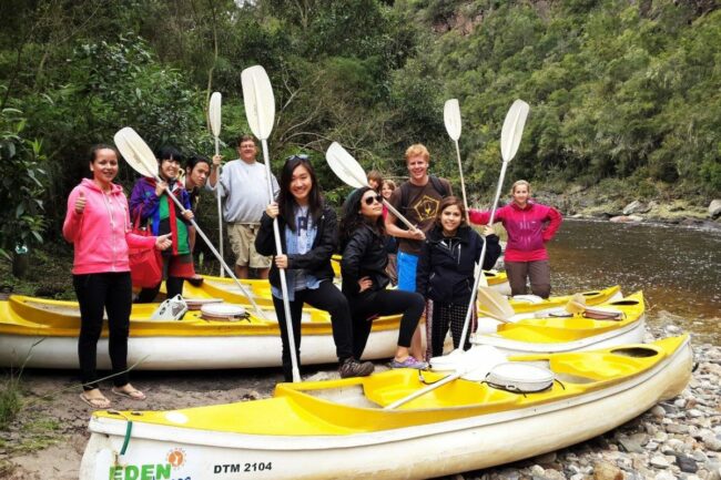 Group of young people pose with canoes next to river in Wilderness South Africa.