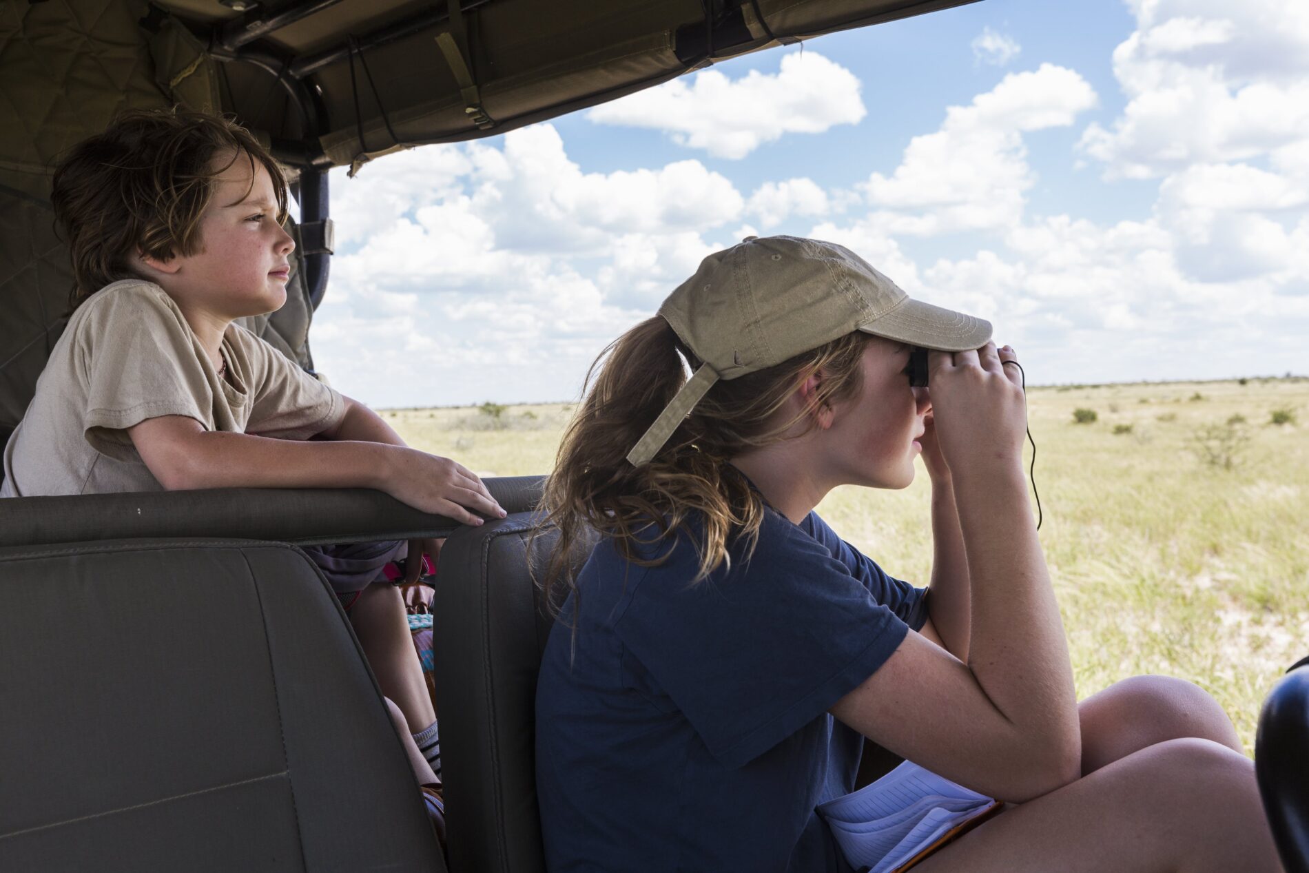 Young brother and sister in safari vehicle looking for animals.