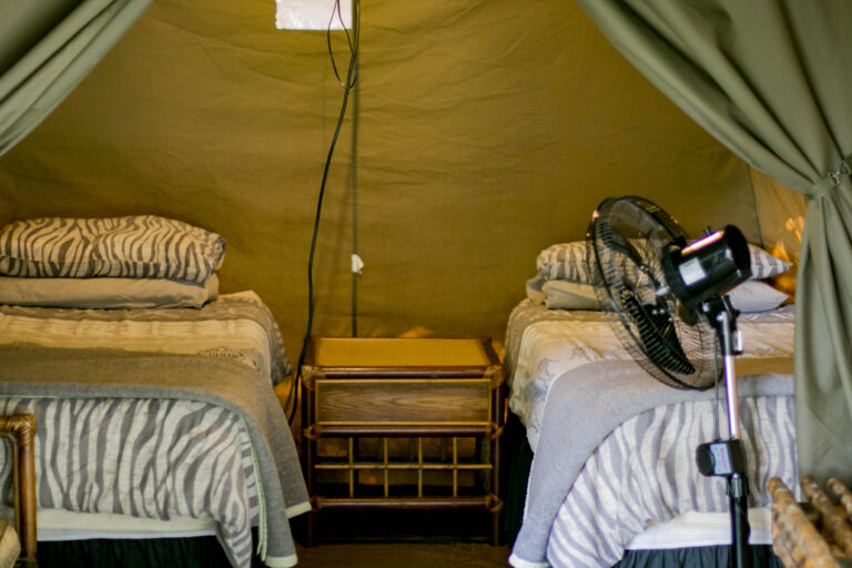 inside of a permanent tent with twin beds, a bedside cabinet and fan