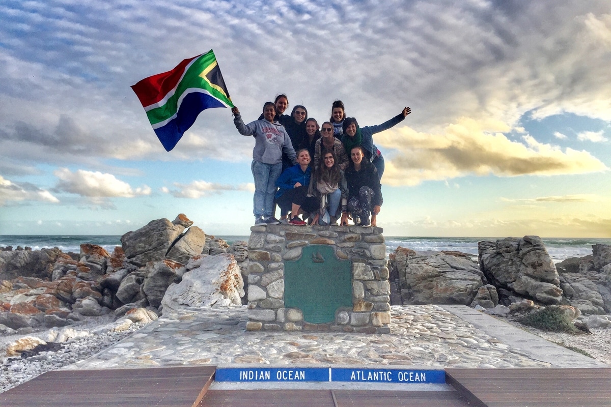 a group of tourists posing with the south african flag at the southern tip of africa