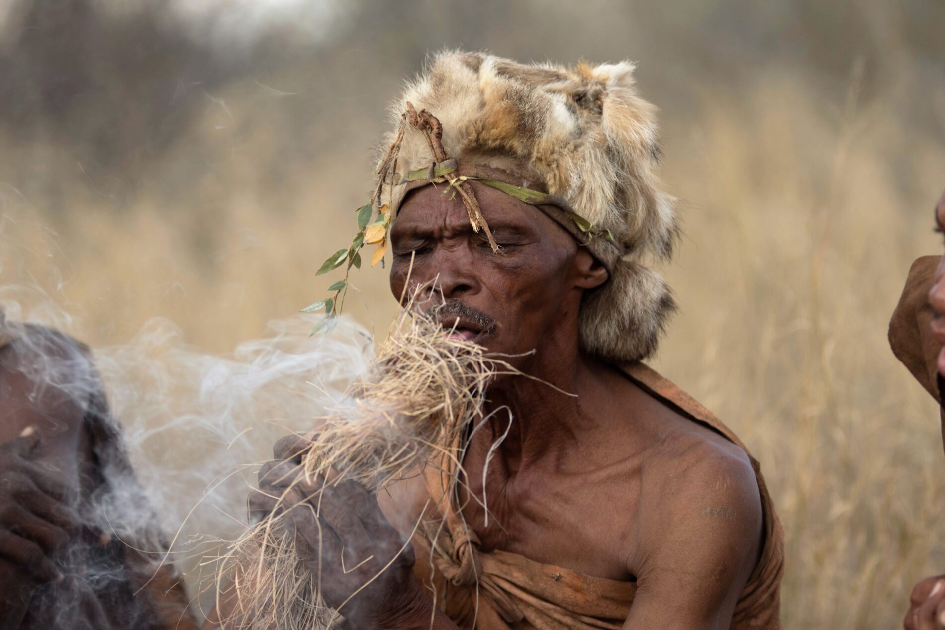 tribal man wearing traditional clothes blowing on a bunch of dried grass to create a fire