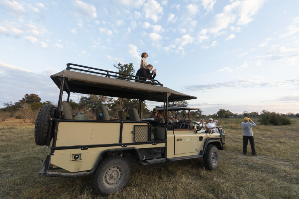 a safari vehicle with two people on top of it looking out at the view with the bush in the background
