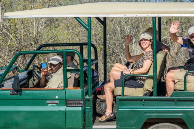 a safari vehicle with the tourists and tour guide waving at the camera