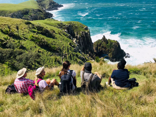 a group of hikers sitting in a field looking out over the water