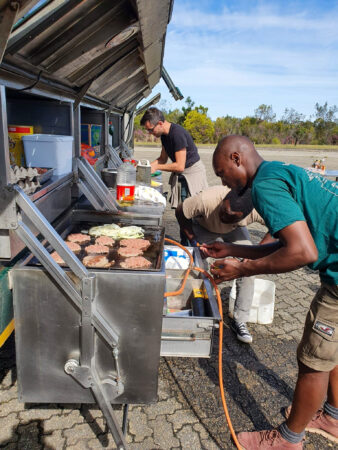 two men leaning over making food at the side of a tour vehicle