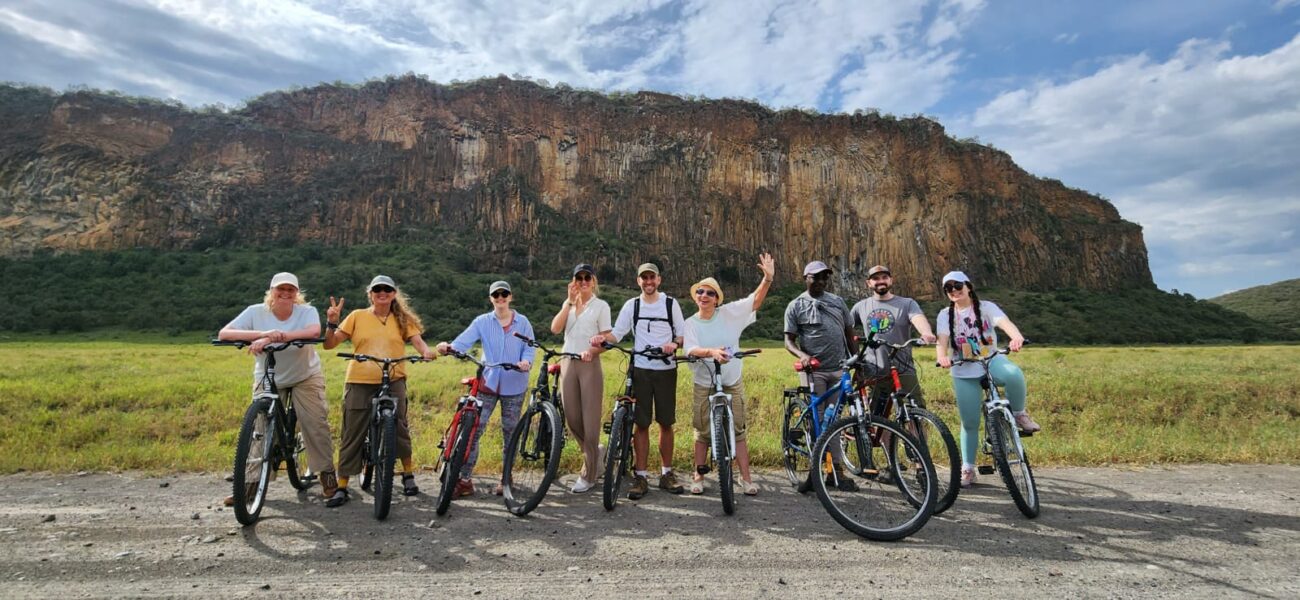 people posing next to their bicycles in front of a mountain while on a tour