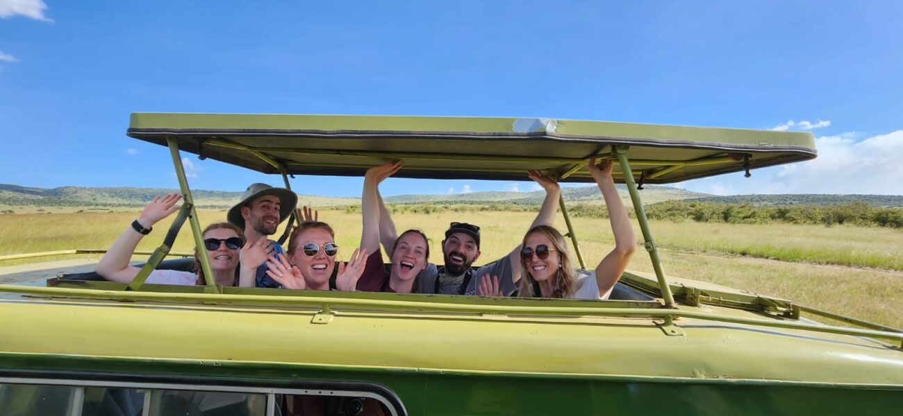 a group of tourists in a safari vehicle with their hands in the air