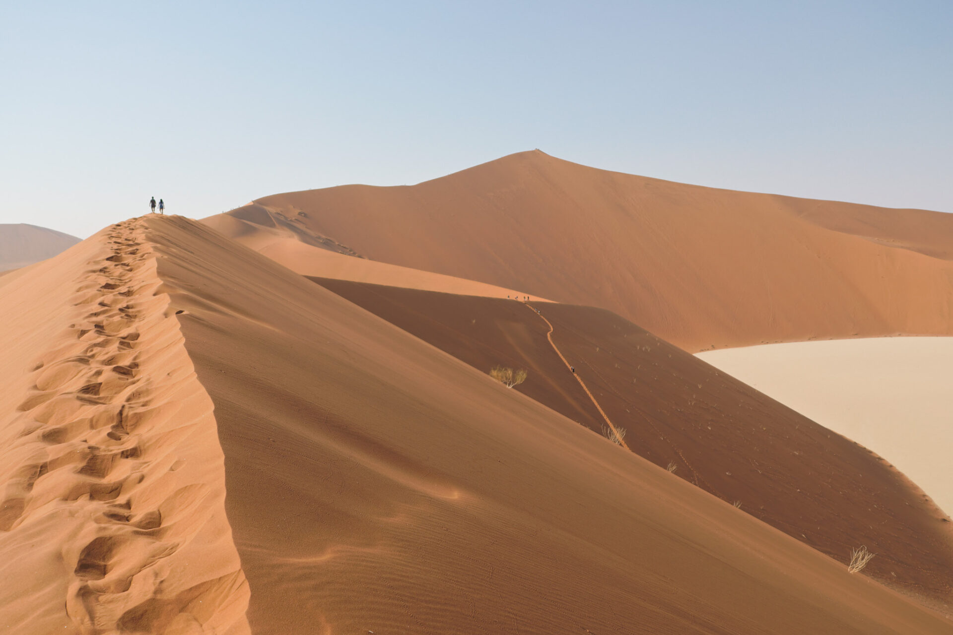 two people walking on a dune in the distance