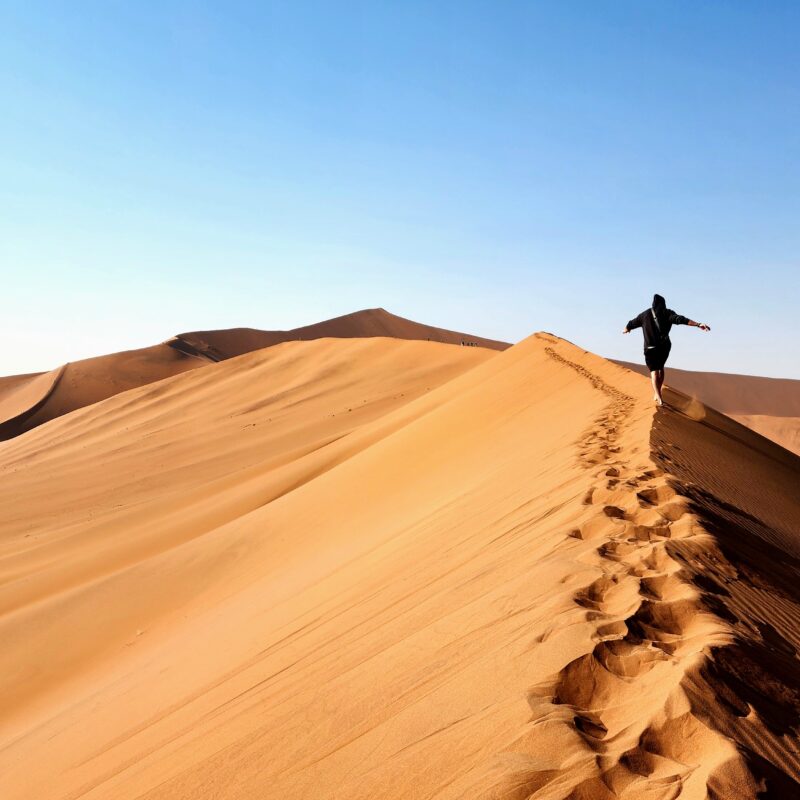 Man running along top of dune in Namibian desert.