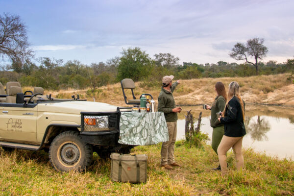 People enjoying coffee on the banks of Sabi River next to safari vehicle.