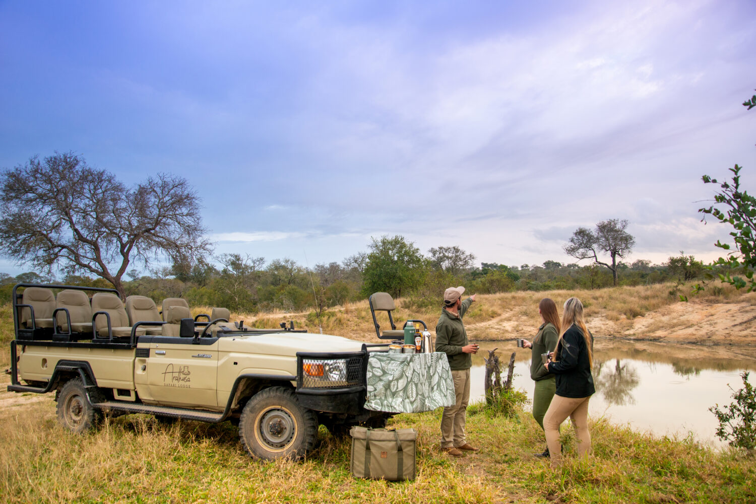People enjoying coffee on the banks of Sabi River next to safari vehicle.