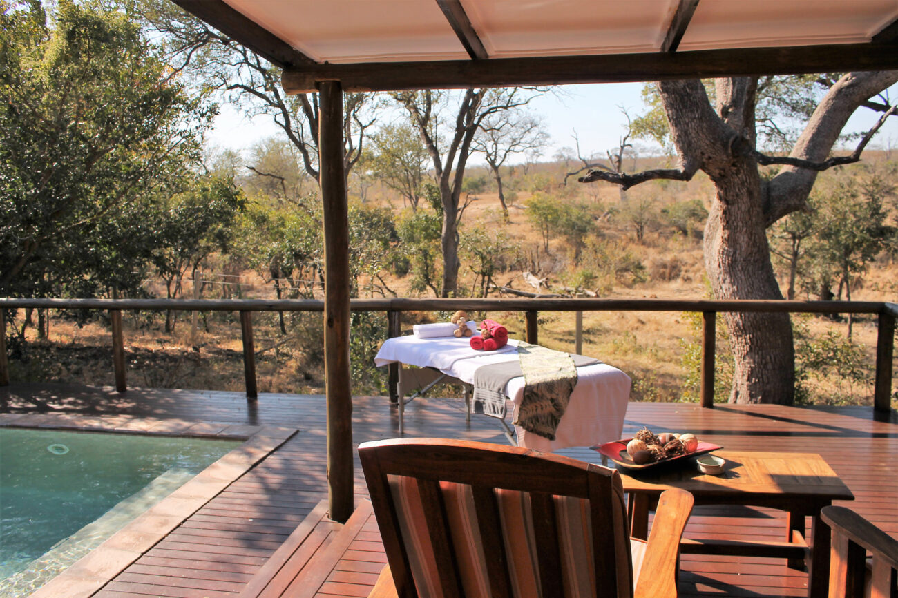 massage table set up on a patio with a swimming pool and beautiful view of the bush