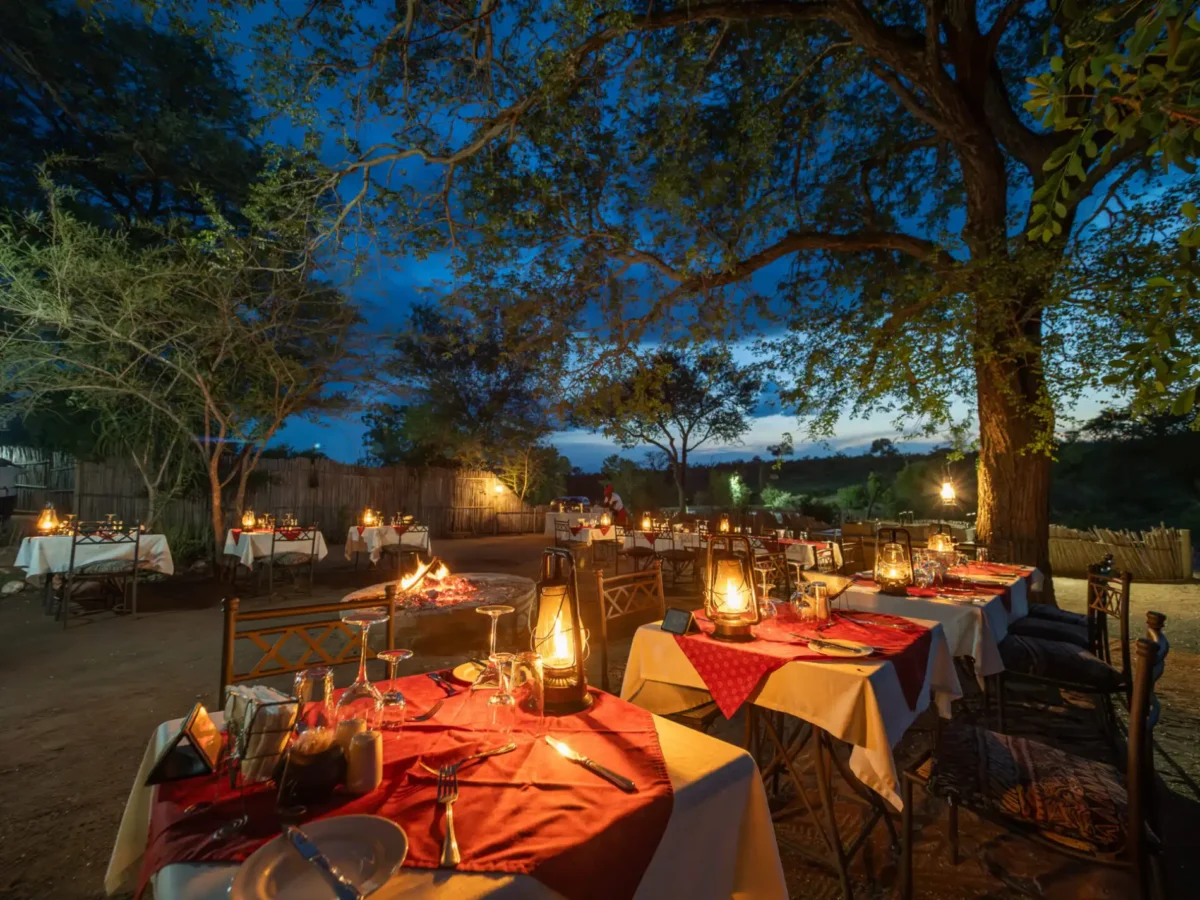 Set dining tables placed around burning fire at safari lodge.