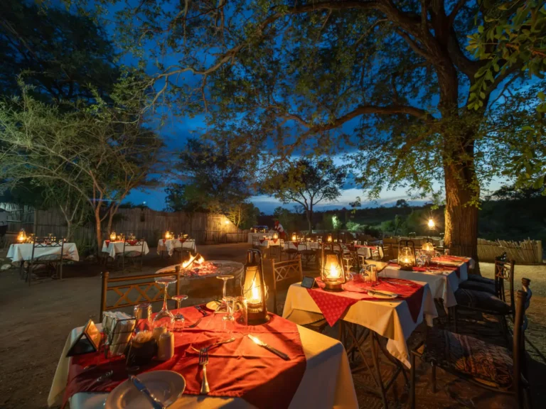 Set dining tables placed around burning fire at safari lodge.