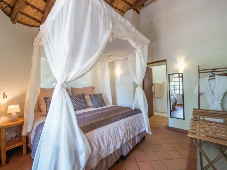 safari-style bedroom with a thatched roof, featuring a luxurious four-poster bed with mosquito netting.