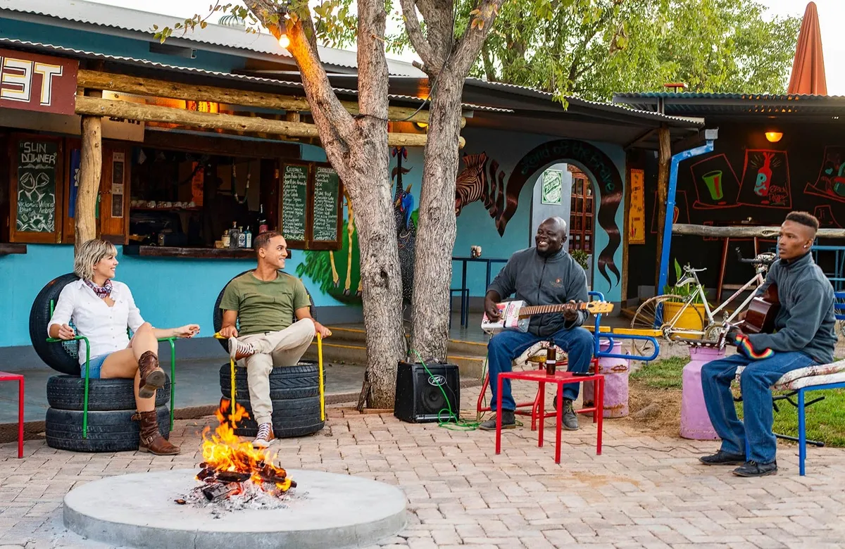 2 men playing guitar next to a fireplace while 2 other people watch