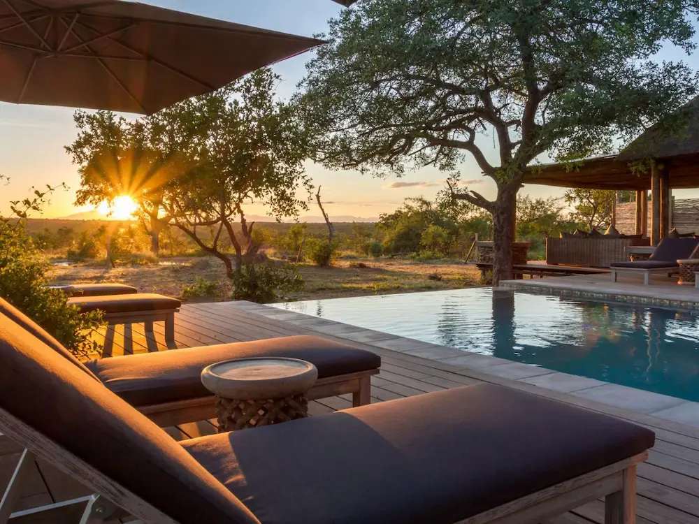 swimming area with sun loungers with the sun setting behind them